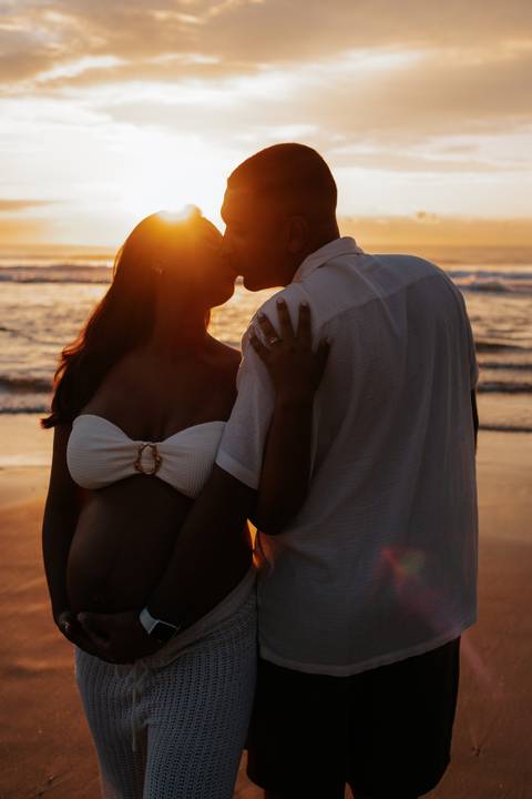 Foto do casal se beijando aproveitando a luz do sol na praia.'