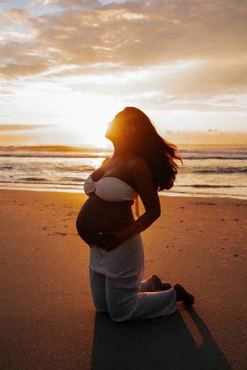 Foto da silhueta da gestante na beira do mar no nascer do sol.'