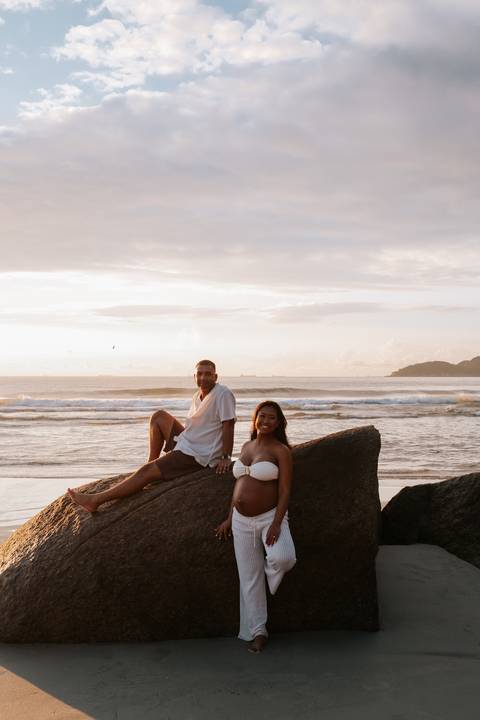 Foto do casal sentado nas rochas da praia durante o amanhecer.'