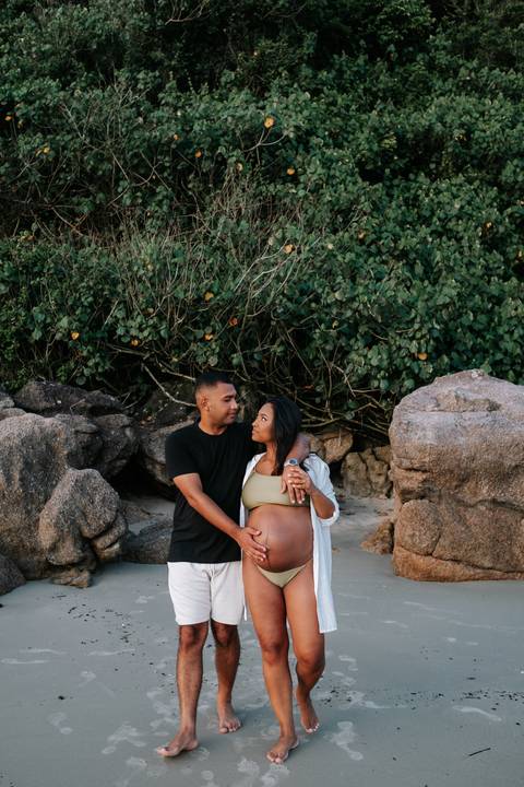 Foto do casal abraçado próximo às rochas em ensaio gestante externo.'