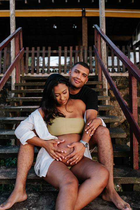 Foto do casal sentado nos degraus da escada na praia em momento afetivo.'