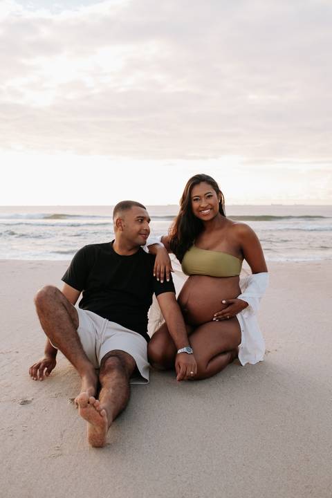 Foto do casal sentado na areia da praia durante o ensaio documental.'