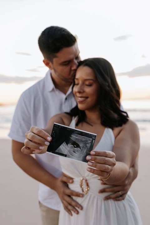 Foto de detalhe da imagem do ultrassom segurada pelos pais.'