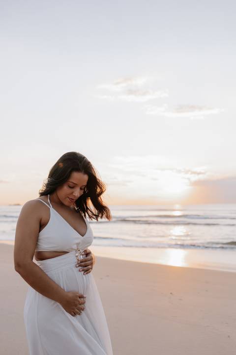 Foto da gestante com nascer do sol no mar de fundo. '