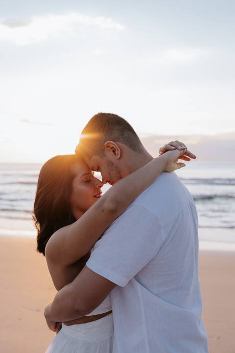 Foto do casal abraçado com o sol brilhando entre os dois.'
