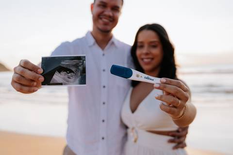 Foto do casal exibindo o ultrassom e o teste de gravidez positivo.'