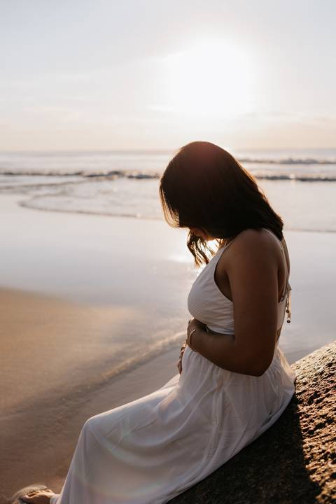 Foto de perfil da gestante em destaque com o reflexo do sol na água.'