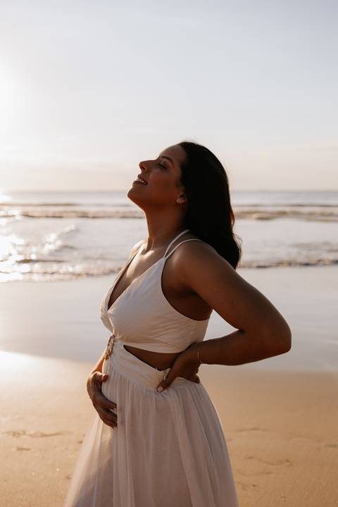 Foto da gestante sorrindo em destaque com o sol ao fundo.'