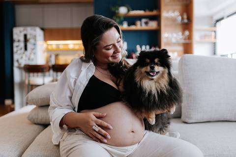 Foto da gestante sorrindo com o cão de estimação no colo.'