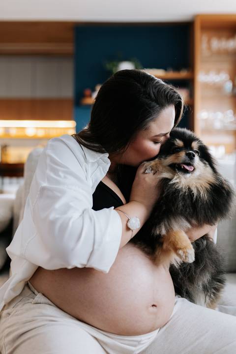 Foto da gestante beijando a cabeça do cão da família em momento afetivo.'