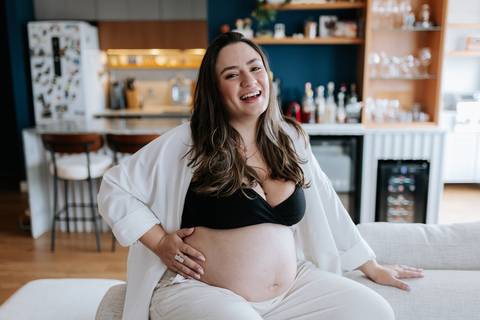 Foto da gestante sorrindo com look preto e branco no ambiente de casa.'