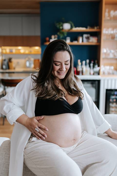 Foto da gestante acariciando a barriga sentada no sofá da sala.'
