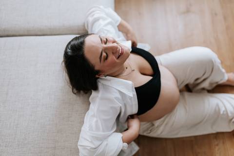 Foto em ângulo superior da gestante relaxada no tapete da sala.'