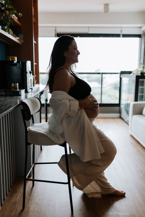 Foto da silhueta da gestante sentada na banqueta da cozinha.'