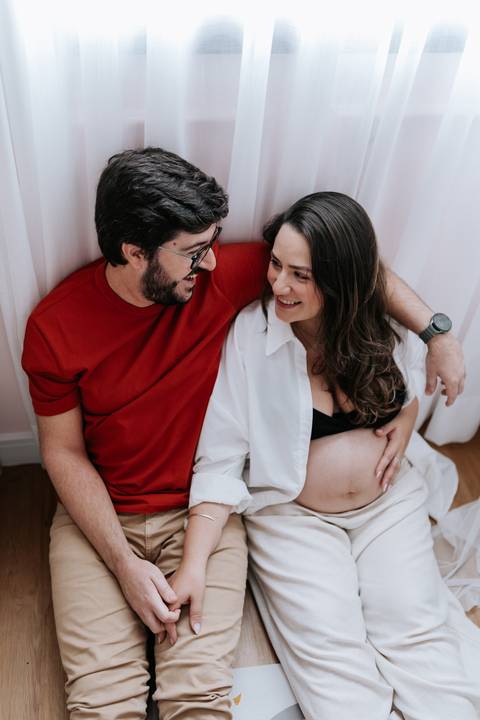 Foto aproximada do casal sorrindo no ambiente aconchegante do lar.'