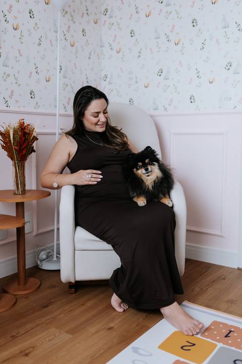 Foto da gestante sentada na poltrona com o cão no colo em momento carinhoso.'
