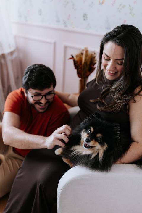 Foto do casal brincando com o cão no quarto do bebê.'