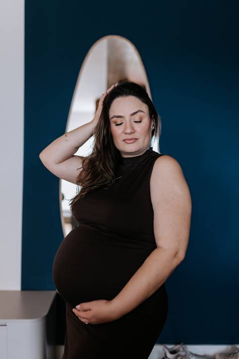 Foto de perfil da gestante com vestido preto destacando a silhueta em casa.'