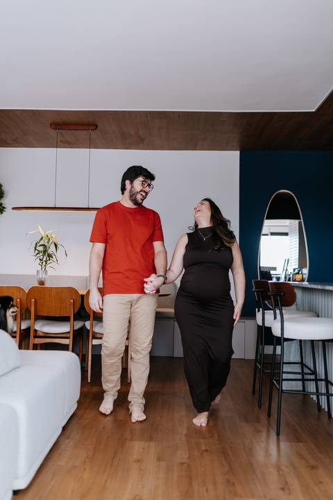 Foto do casal de mãos dadas sorrindo no ambiente da sala de jantar.'