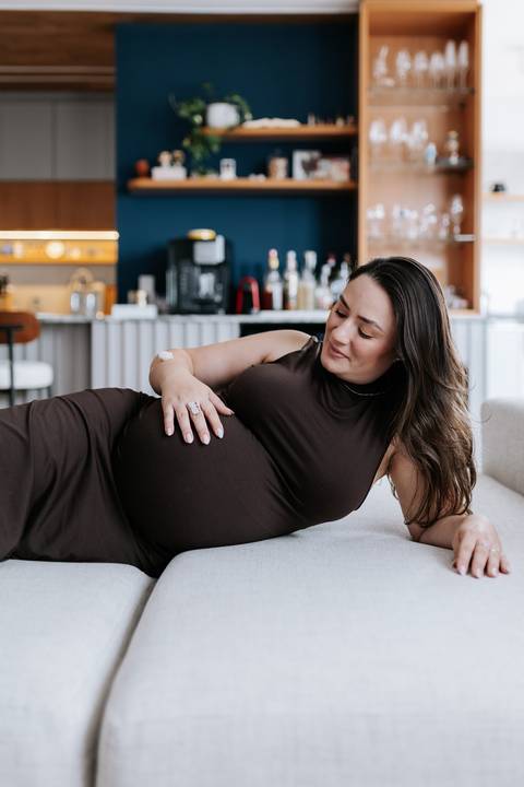 Foto da gestante relaxada no sofá em momento contemplativo.'