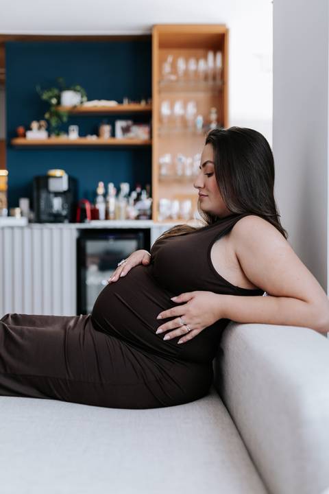 Foto de perfil da gestante sentada no sofá com look minimalista.'