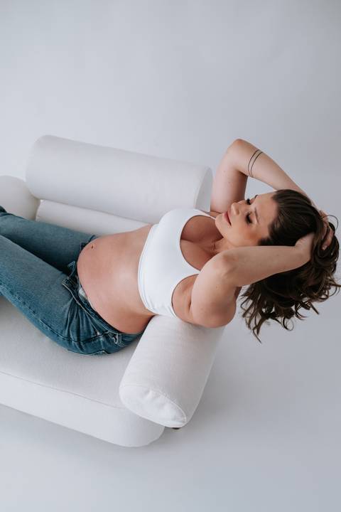 Foto da gestante relaxada no sofá posando para o ensaio de estúdio.'