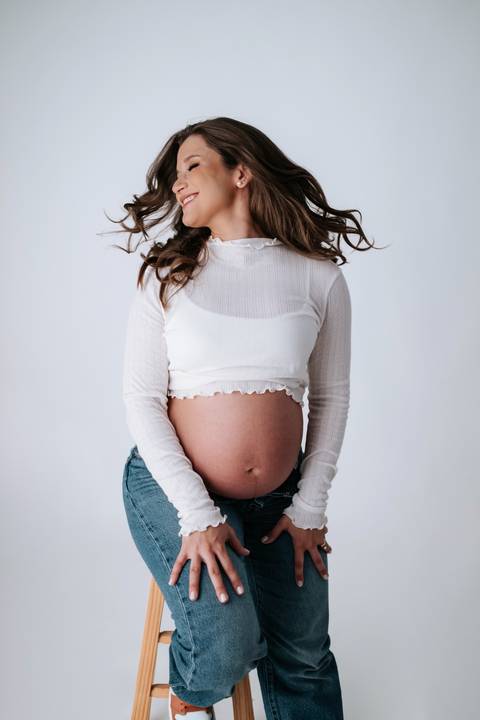 Foto aproximada da barriga da gestante com blusa branca.'