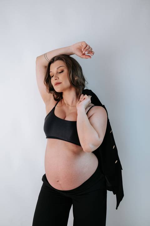 Foto da gestante posando com blazer preto em estilo editorial.'