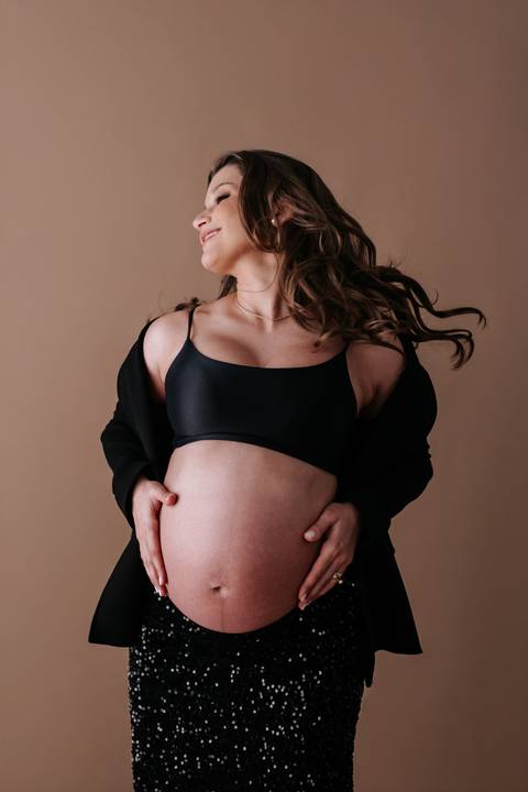 Foto aproximada da gestante sorrindo com as mãos na barriga e luz lateral suave.'