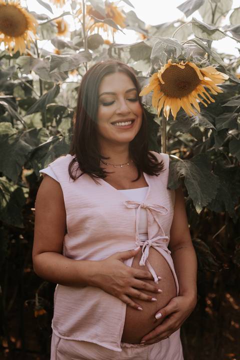 Foto aproximada da gestante sorrindo em destaque no campo de flores.'