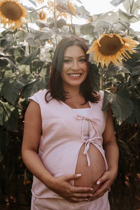 Foto de close da gestante com expressão serena em meio à natureza.'