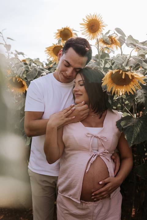 Foto do casal abraçado em momento de carinho no campo de girassóis.'