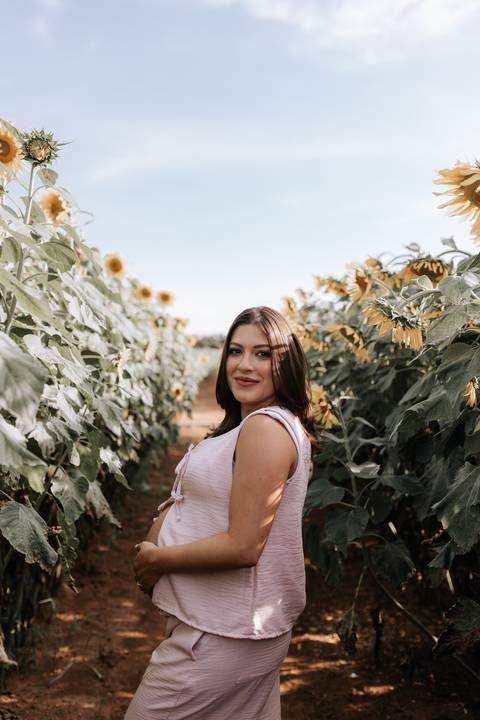Foto de perfil da gestante olhando para a câmera entre as flores amarelas.'