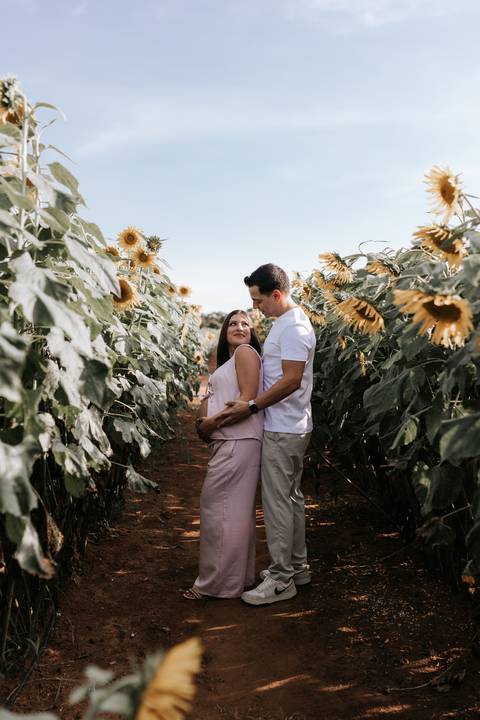 Foto do casal trocando olhares com a barriga de grávida em destaque no campo.'