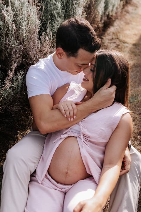 Foto aproximada do casal com os rostos próximos sob a luz natural.'