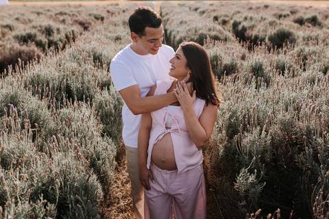 Foto do casal em pé em um campo de lavandas durante o entardecer.'
