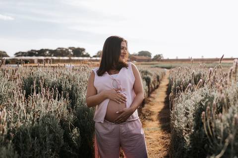 Foto da gestante de perfil caminhando pelo corredor de lavandas.'