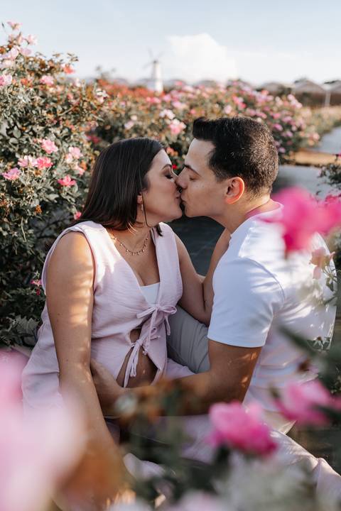 Foto do casal se beijando com flores cor-de-rosa em primeiro plano.'