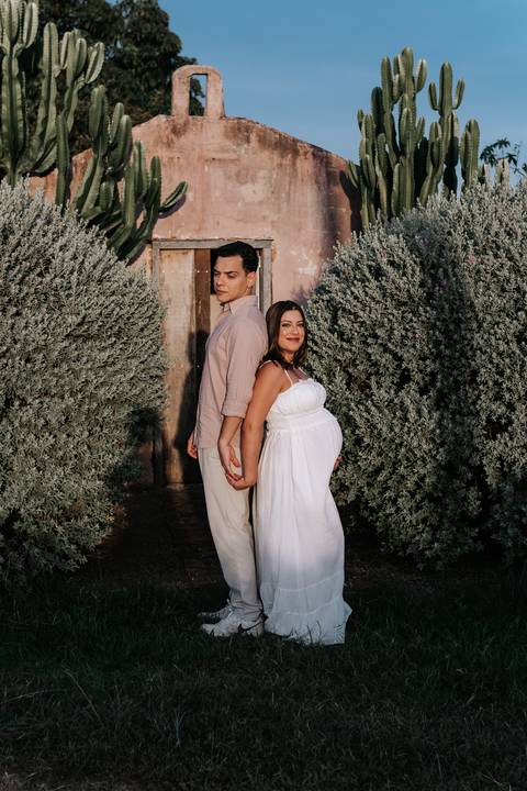Foto do casal de costas um para o outro em frente a uma estrutura rústica.'