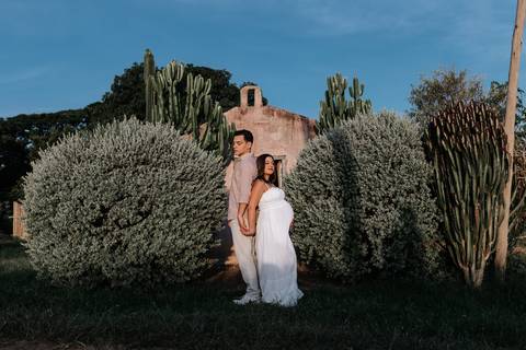 Foto do casal em um jardim com arquitetura antiga e cactos.'