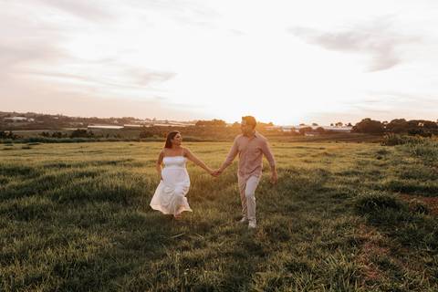 Foto do casal de mãos dadas caminhando no gramado durante o pôr do sol.'