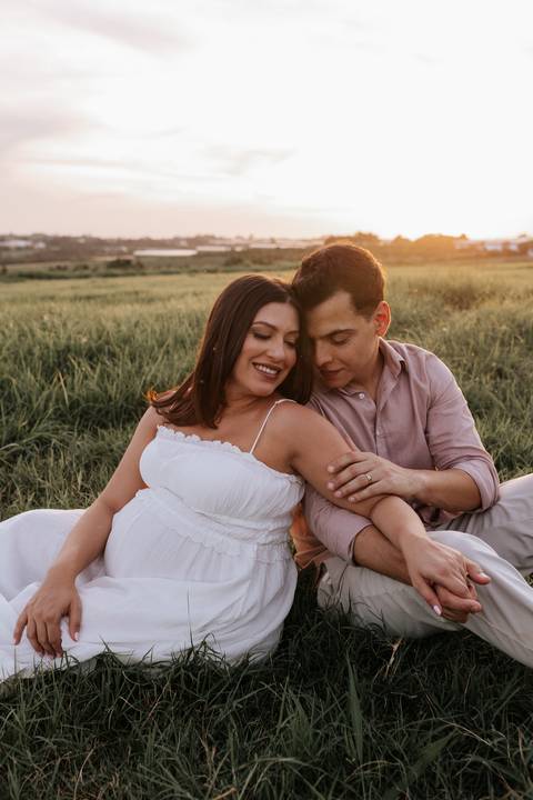 Foto do casal sentado na grama em momento de carinho e risadas.'