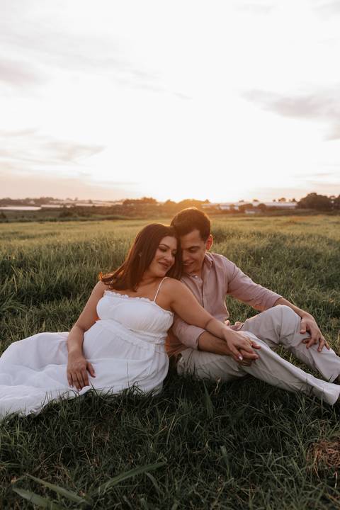 Foto aproximada do casal sentado no campo sob a luz dourada do amanhecer.'