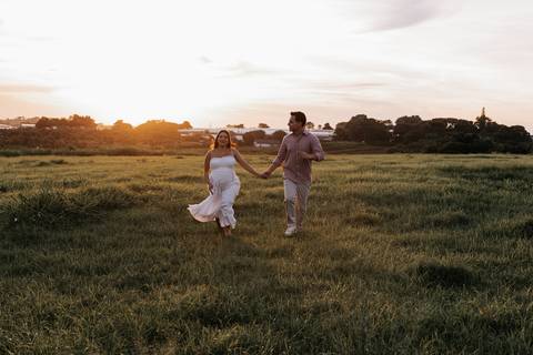 Foto do casal caminhando de mãos dadas em campo aberto com o sol ao fundo.'