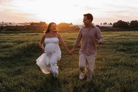 Foto da gestante e o parceiro sorrindo enquanto caminham no gramado.'