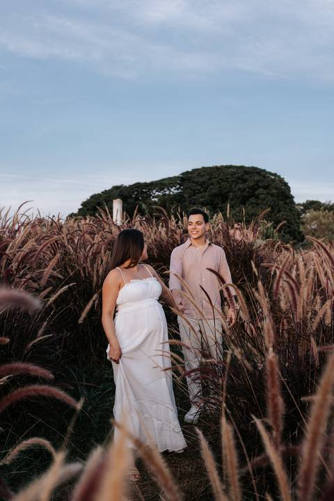 Foto do casal em pé entre a vegetação alta em momento romântico.'