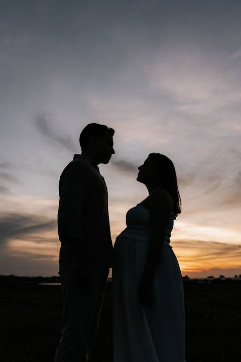 Foto da silhueta do casal frente a frente contra o céu no nascer do sol.'