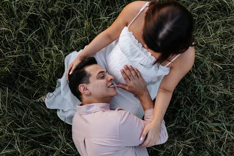 Foto em ângulo superior do pai deitado no colo da gestante no gramado.'