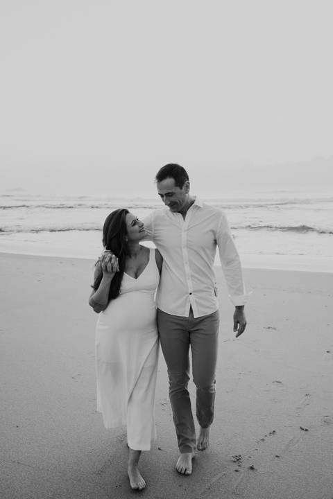Foto em preto e branco do casal sorrindo e caminhando na areia da praia.'