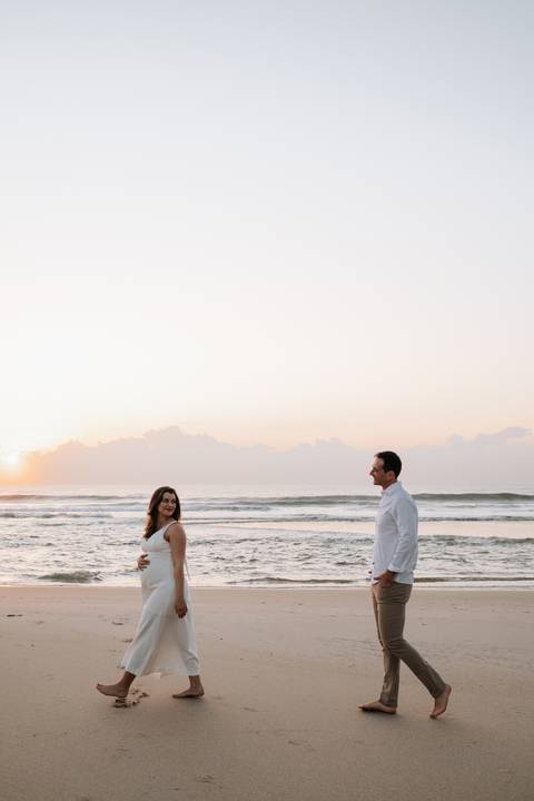 Foto do casal trocando olhares em meio à imensidão da praia no amanhecer.'